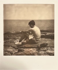 a photo of a man sitting on a rock next to the ocean